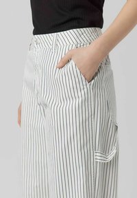 Pantalon blanc à rayures avec des lignes verticales bleu marine. Doté d'une poche latérale et d'une fermeture à bouton, fabriqué en tissu lisse avec une coupe décontractée.