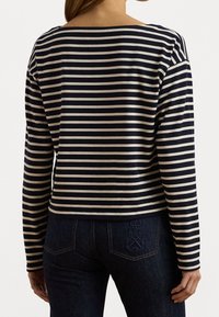 Blusa de rayas azul marino y beige de manga larga con escote ancho; tejido suave; corte relajado; presenta un detalle bordado en la parte posterior.