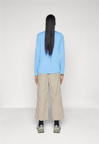 Blue long-sleeve shirt, light beige wide-leg pants, gray sneakers, and black socks. Hair is long and straight, styled down the back.
