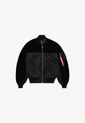 Črn bombnik s flisom na zgornjem delu telesa in rokavih, sprednjim zadrgo, dvema stranskima žepoma in rdečo oznako "Remove Before Flight" na žepu levega rokava.