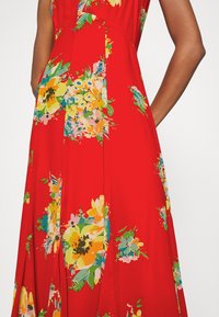 Röd blommig klänning med ärmlös design, livfulla mångfärgade blommönster och en flödande silhuett med sidofickor.