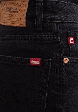 Juoda džinsų medžiaga su ruda odos etiketė su "BIG STAR" ženklu, raudonais siūlų akcentais ir vario spalvos sagte.