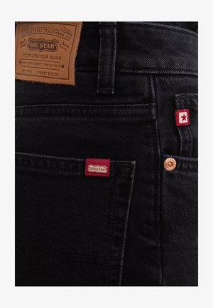 Zwarte denim jeans met een bruine leren patch met het "BIG STAR" label, rode stiksels en een koperkleurige knop.