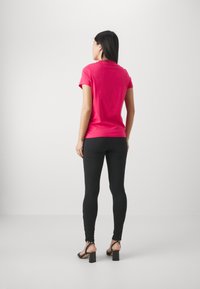 Fitted rosa bomull T-skjorte med korte ermer, kombinert med svarte leggings og svarte høyhælte sandaler, sett fra baksiden.