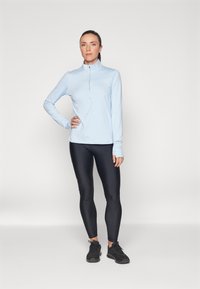 Ljust blå långärmad skjorta med en kvarts dragkedja, i kombination med svarta leggings och svarta sneakers. Slät tyg, figurnära design.