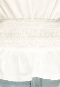 Gros plan de tissu blanc froncé avec des détails smocks élastiques au-dessus d'un jean en denim bleu.