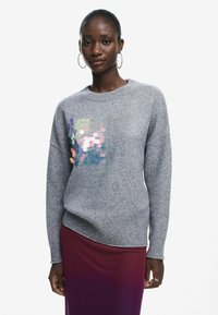 Pull en tricot gris avec un col rond et des manches longues, présentant des détails en sequins irisés sur le devant et un ourlet côtelé.