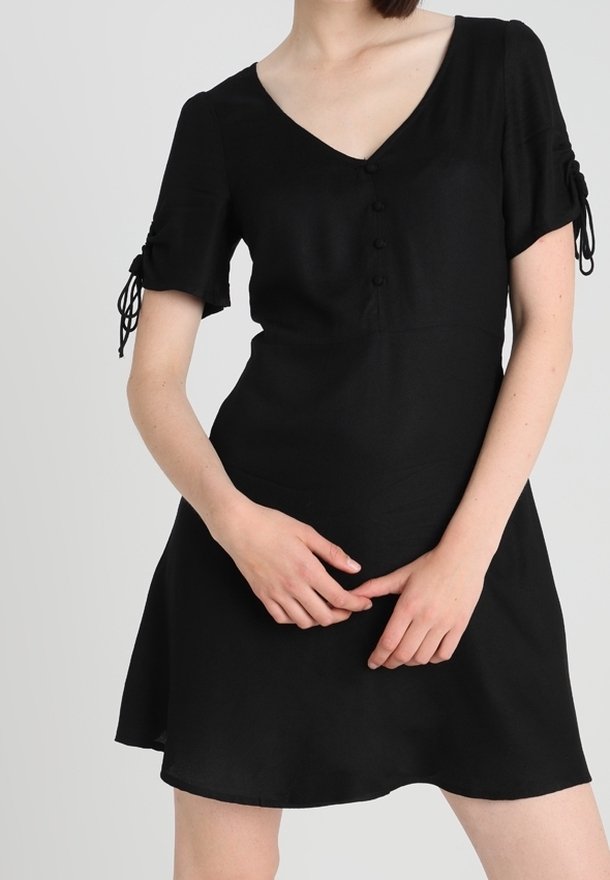 Robe noire à manches courtes avec un décolleté en V, mettant en avant des détails de boutons et des accents à nouer sur les manches. Tissu lisse ; forme de jupe évasée.