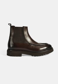 Bottines Chelsea en cuir marron avec des panneaux élastiques sur les côtés, bout rond et semelle en caoutchouc texturée. Comprend un accent de couture décoratif près du bout.