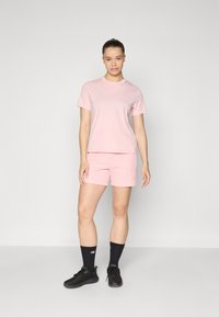 T-shirt rose à manches courtes et shorts assortis, en tissu doux, arborant un petit logo. Porté avec des chaussures de sport noires et des chaussettes.