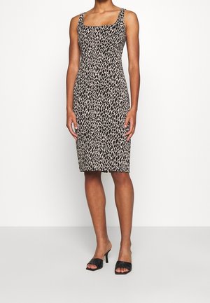 Donna che indossa un vestito senza maniche fino al ginocchio con stampa leopardata e sandali neri con tacco e punta aperta, in piedi davanti a uno sfondo bianco semplice.
