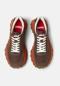 Sneaker marroni con una parte superiore in tessuto testurizzato, lacci bianchi, accenti arancioni audaci e suola in gomma spessa con un motivo di battistrada a tasselli.