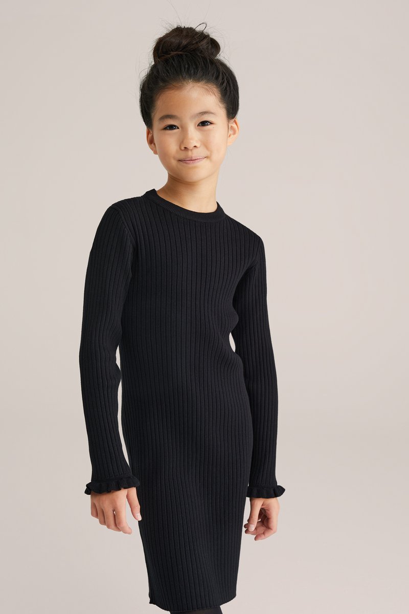 Svart ribbad stickad klänning med långa ärmar, med en rund halsringning och volangdetaljer vid ärmsluten. Slät textur, figurnära design.