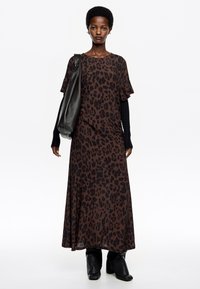 Maxikleid mit Leopardenmuster in Dunkelbraun und Schwarz, mit kurzen Ärmeln, kombiniert mit einer schwarzen Tasche und Stiefeletten mit Absatz, aus glattem Stoff.