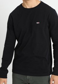 Schwarzes Langarm-T-Shirt aus Baumwollmischung, mit einem runden Ausschnitt und kleinem Logo in Rot, Weiß und Blau auf der Brust.
