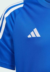Camiseta deportiva azul hecha de tela suave, que presenta tres franjas blancas a lo largo de los hombros y un logo bordado en blanco en el pecho.