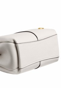 Sac à main en cuir blanc texturé avec des bords arrondis et une bordure noire, montré en gros plan en vue latérale angulée.