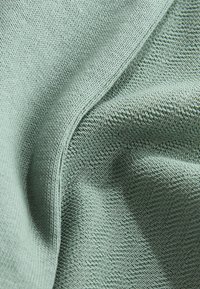 Textured knit fabric in soft green, featuring a smooth surface with a slight sheen and even stitching, showcasing subtle patterns.