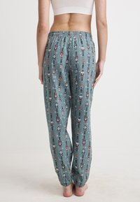 Ljusblå pyjamasbyxor med nötknäpparmönster, elastisk midja och avsmalnande ben. Materialet verkar mjukt med en slät yta.