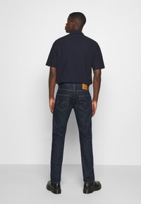 Jeans de mezclilla azul marino con un parche de cuero en la parte trasera, combinados con una camisa de manga corta azul marino. Textura suave, corte regular y diseño clásico.