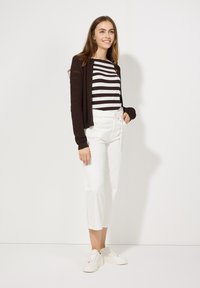 Bruine gebreide cardigan, zwart-wit gestreept shirt, witte broek met hoge taille en witte sneakers. Rechte pasvorm met gedetailleerde texturen.