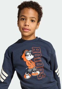 Marineblauwe sweatshirt met een cartoon muis graphic; oranje accenten; drie witte strepen op de mouwen; casual, moderne pasvorm; katoenmix materiaal.