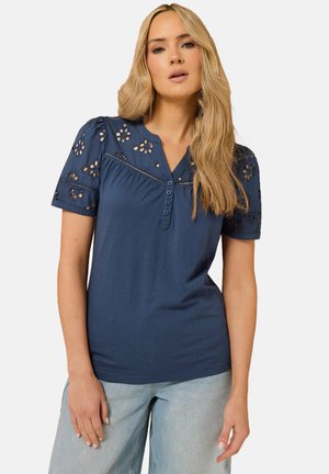 T-shirt en coton bleu marine avec de courtes manches bouffantes, broderie florale en œillets, encolure en V et patte de boutonnage à trois boutons sur le devant.