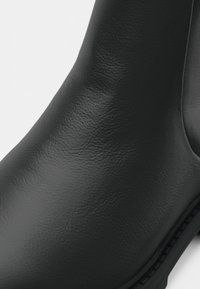 Botín de piel negra hasta el tobillo con una textura suave, forma redondeada y un detalle de costura mínima a lo largo de la suela.