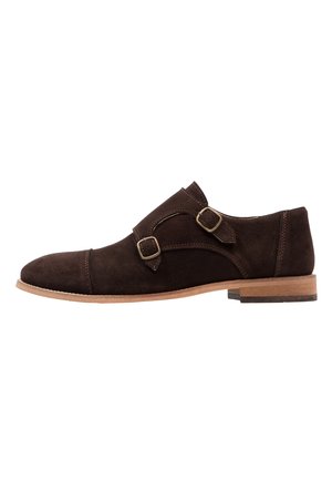 Dunkelbrauner Wildleder-Doppelmokassins-Schuh mit Holzsohle und runder Zehenform, seitlich auf weißem Hintergrund dargestellt.