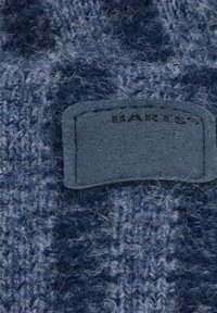 Close-up of blue and gray fuzzy knit fabric with a stitched rectangular leather patch labeled "BARTS."