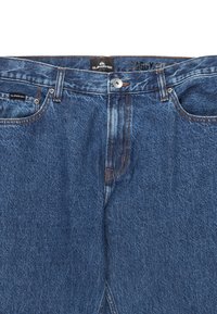 Sin jeans denim blå med løs passform, lukning med knap og kontrasterende syninger. Har forlommer og et mærke indeni taljebåndet.
