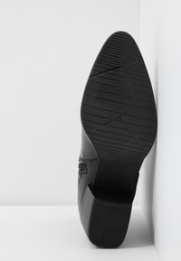 Semelle de chaussure en cuir noir avec talon carré, motif de semelle texturé et détail de couture visible sur le côté.