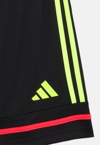 Mustad spordipüksid, millel on kolm neoonkollast triipu, neoonkollane Adidas logo ja punane rõhutusriba ääres.