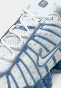 Λευκό και μπλε αθλητικό παπούτσι Nike σε κοντινή λήψη που δείχνει υφασμάτινο πλέγμα, κορδόνια, υφή σόλας και το λογότυπο swoosh της Nike στο πλάι.