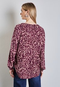 Langermige blouse met een paars en roze abstract patroon, met gathered details bij de halslijn en elastische manchetten.