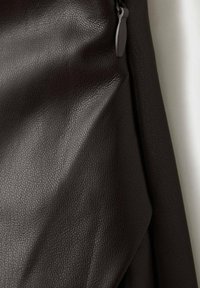 Material maro texturat din piele ecologică cu o textură fină, având un detaliu cu fermoar negru și elemente de design drapate.