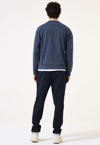 Navyblauwe trui met een gestructureerde afwerking, ronde hals, en geribde zoom, gecombineerd met donkerblauwe joggingsbroeken en lichtgekleurde sneakers.