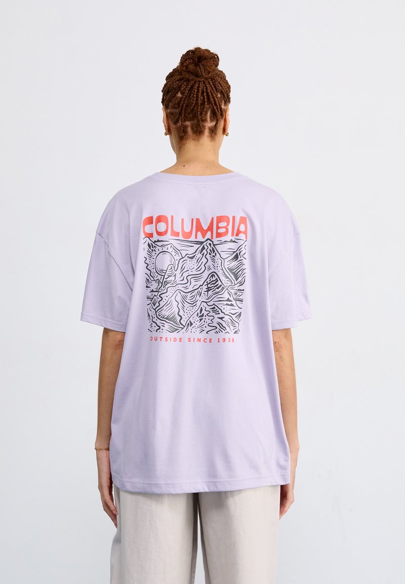 Maglietta oversize lavanda con un design grafico di montagne e la scritta "COLUMBIA" in rosso sul retro. Materiale in cotone.