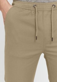 Beige joggerbyxor med elastisk midja, snörning, sidofickor och en mjuk, slät textur.
