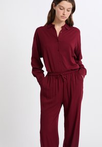 Bordeaux shirt met knopen en een kraag, gecombineerd met bijpassende loszittende broek met elastische taille. Zachte stof met een gladde textuur.