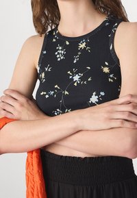 Top in jersey a righe di colore nero con stampa floreale, con scollatura rotonda e senza maniche. Presenta delicati fiori blu e gialli.