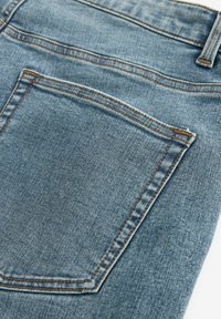 Jeans de denim azul claro con una textura desgastada, que cuentan con un bolsillo trasero delineado por un pespunte naranja en contraste.