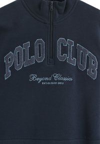 Maglione navy con colletto alto, chiusura a zip a un quarto e design ricamato "POLO CLUB". Texture morbida con dettagli a contrasto.