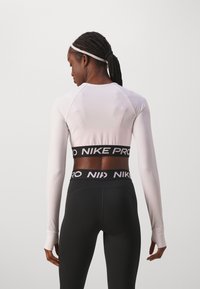 Haut de sport à manches longues blanc avec une coupe ajustée et des trous pour les pouces, associé à un legging noir avec une taille ornée d'un logo prominent.