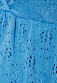 Tecido azul com padrões de flores bordadas e pequenos recortes. Textura suave com um leve brilho, levemente franzido na cintura.