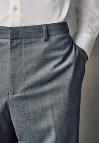 Pantalones grises a medida con una textura suave, con un frente plano y bolsillos laterales, combinados con una camisa blanca de botones.