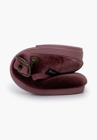 Zapatilla de terciopelo burdeos, diseño flexible, forma redondeada, con un acento de botón de latón y suela texturizada para un mejor agarre.