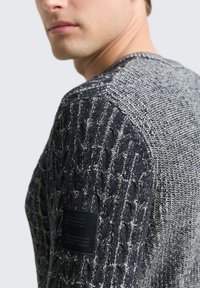 Strickpullover mit strukturiertem Zopfmuster in Dunkelgrau und Hellgrau, mit einem schwarzen Markenlabel auf der linken Schulter.