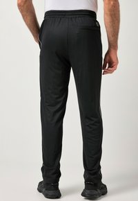 Musta urheiluhousut, joissa on teksturoitu, hengittävä materiaali, istuva malli, valkoiset sivuraidat ja takatasku.