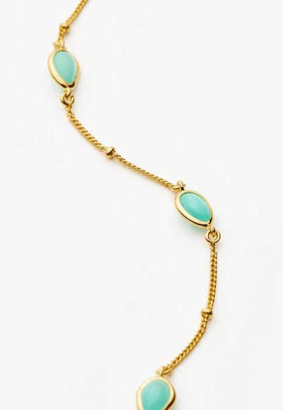 Χρυσό κολιέ αλυσίδα με τρεις οβάλ πέτρες τιρκουάζ τοποθετημένες ομοιόμορφα κατά μήκος της αλυσίδας πάνω σε λευκό φόντο.